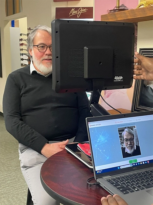 A man seated in front of a Spark Machine gets fitted for glasses.