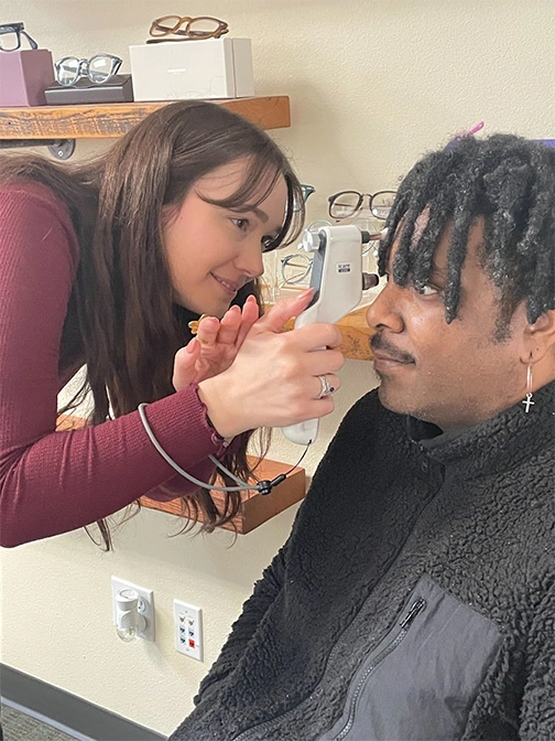 A woman holds a tonometer to a man's eye.