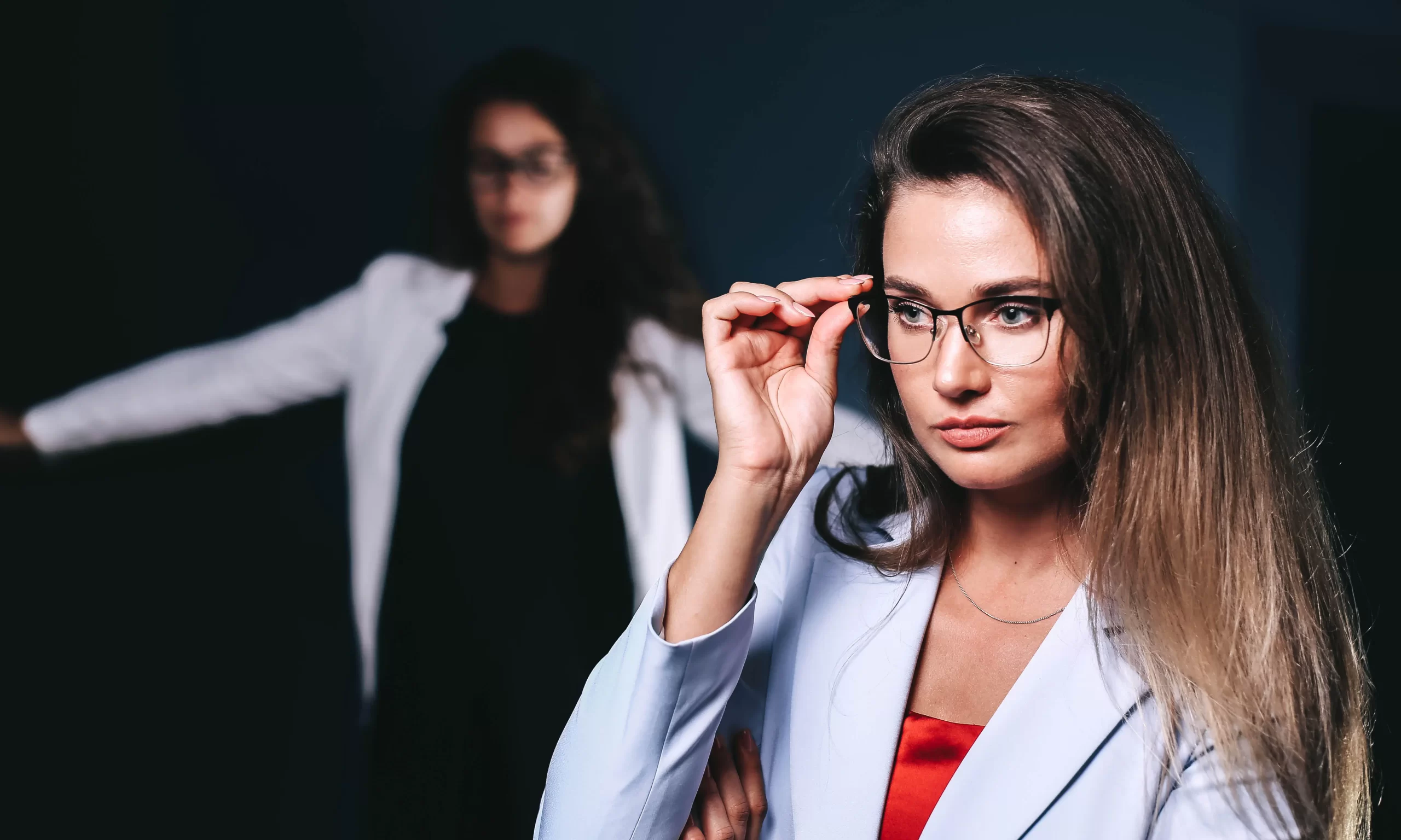 A woman in a suit poses while wearing glasses.